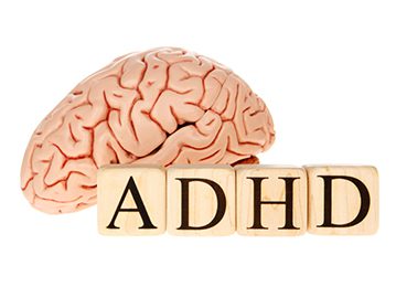 the word adhd spelled with scrabble blocks in front of a brain