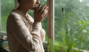 a woman standing in front of a window holding a cup