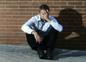 a man sitting on the ground next to a brick wall