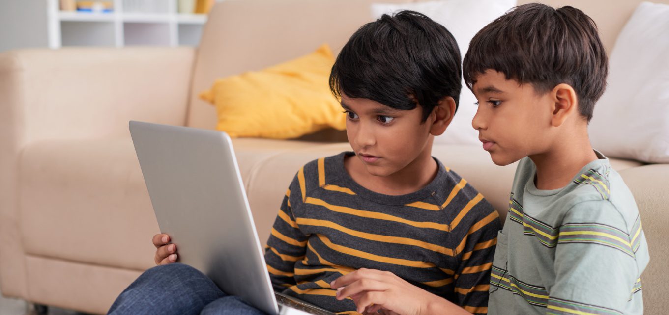 two young boys sitting on the floor looking at a laptop