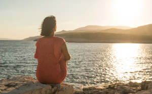 a woman sitting on a rock looking out at the water