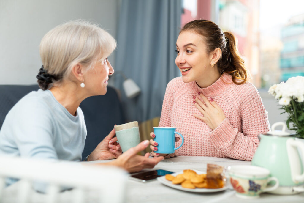 An older woman and her adult daughter talking over coffee at a kitchen table