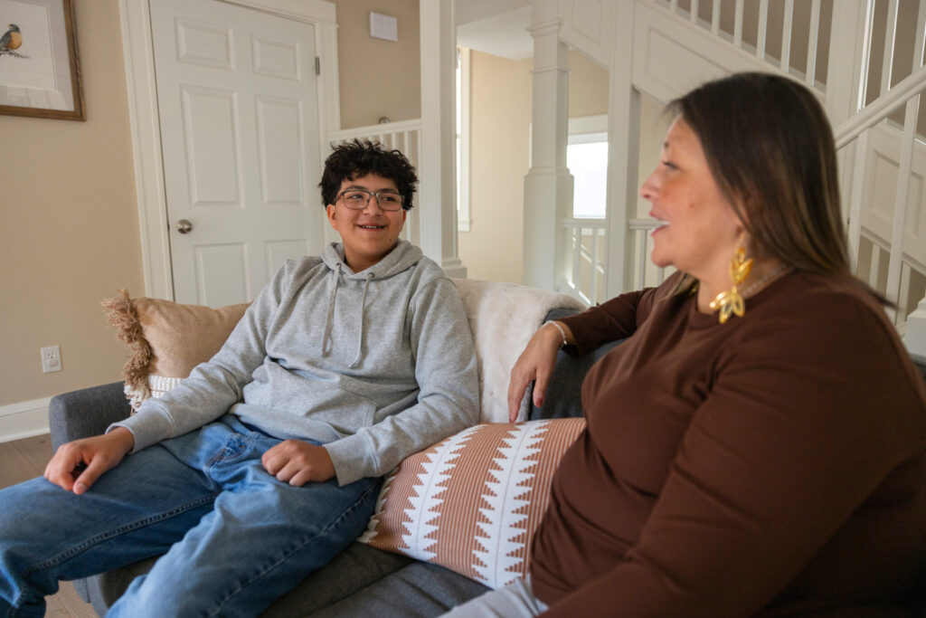 A mother and her teenage son sitting together on a living room sofa in conversation